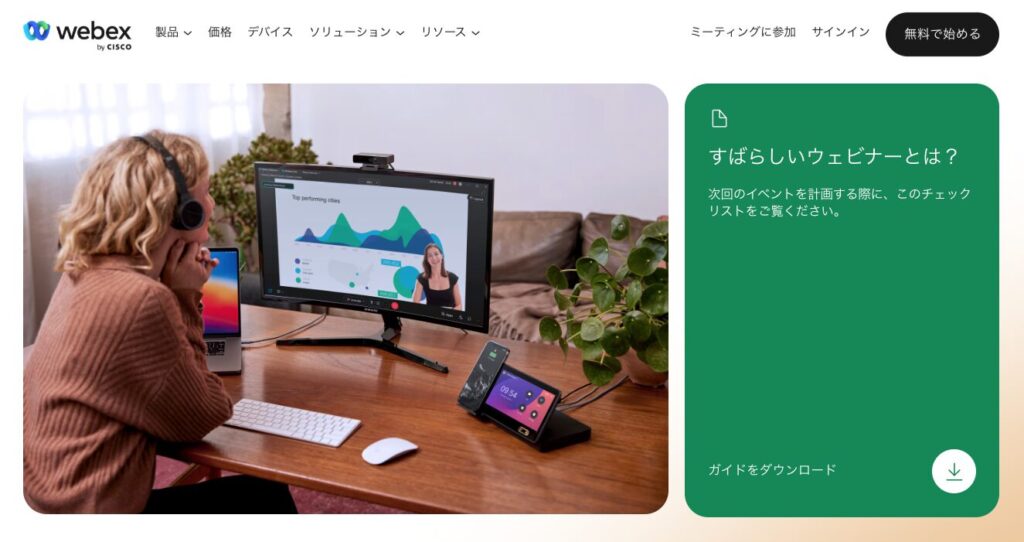 Person with headset watching a monitor displaying graphs during a video call at a wooden desk with laptop and phone dock nearby