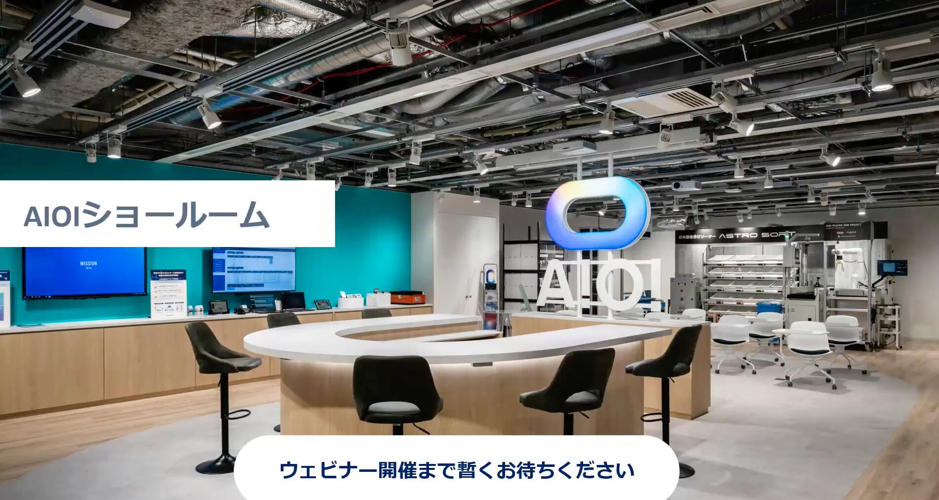 AIO showroom interior with a circular white information counter, black stools, teal wall, and a large illuminated AIO logo.